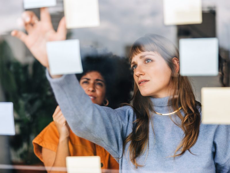 Creative businesswomen brainstorming using sticky notes. Young businesswomen discussing their business ideas during a meeting. Two female entrepreneurs working as a team in a modern office.